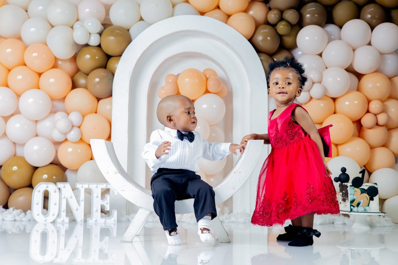 A young boy and girl dressed up in front of a balloon backdrop
